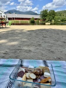 A mini charcuterie board picnic by a pond in Waterville Valley, with mountains in the background.