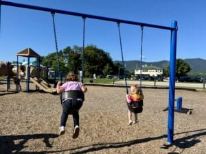 Children swinging at Schouler Park with mountain views in the background.