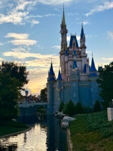 Cinderella Castle at Magic Kingdom, beautifully illuminated by the soft glow of the sunset, with its reflection in the surrounding water.