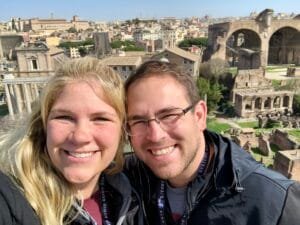 Couple smiling with the ancient ruins of the Roman Forum in Rome, Italy, in the background.