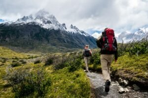 Two hikers with backpacks trekking a scenic mountain trail in Patagonia with towering snow-capped peaks in the background.